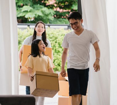 Happy Asian young family bought new house. Japanese Mom, Dad, and child smiling happy hold cardboard boxes for move object walking into big modern home. New real estate dwelling, loan and mortgage.