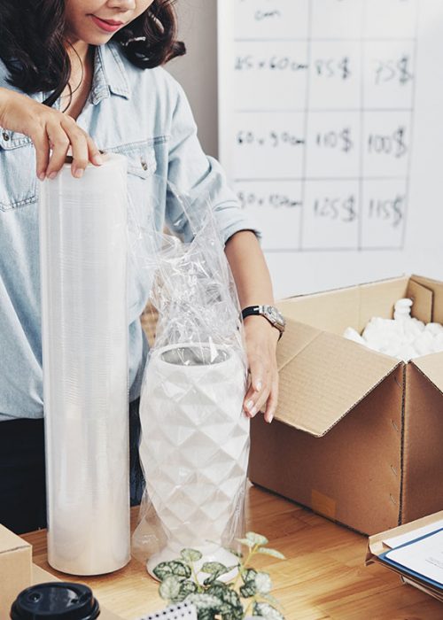 Young office worker packing beautiful vase in cardboard box